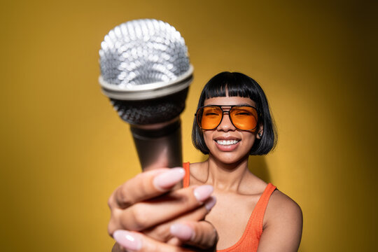 Young Latin woman holding microphone on yellow background