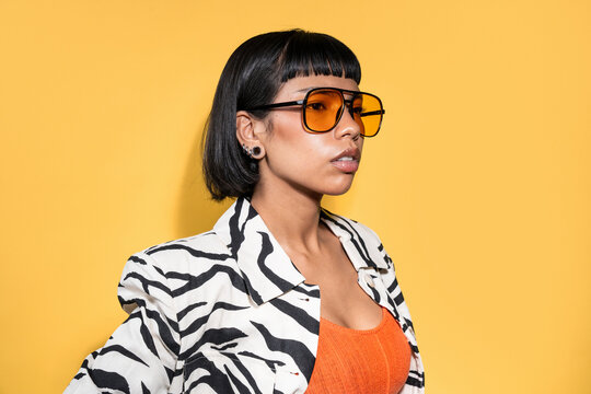 Stylish Latin young woman in orange sunglasses on yellow