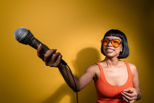 Smiling Latin young woman holding microphone on yellow wall