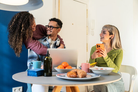 Young couple with flatmate chatting at home table