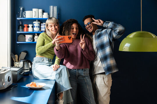 Multiethnic flatmates taking a cheerful kitchen selfie
