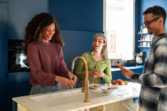Multiethnic flatmates cooking and chatting in modern kitchen