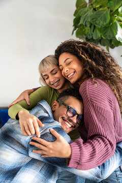 Multiethnic flatmates hugging together on cozy sofa