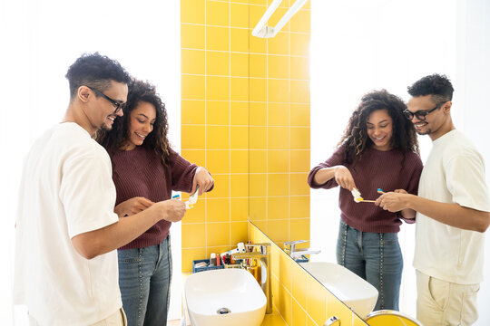 Latin couple brushing teeth together in bright bathroom