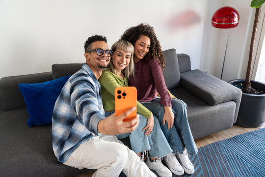 Multiethnic flatmates taking selfie on living room sofa