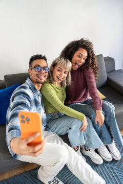 Multiethnic flatmates taking selfie on sofa at home
