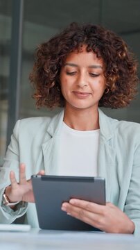 Smiling latin businesswoman sitting at office desk and using tablet in workspace, communication. Young indian woman holding tab screen device for work online. Technology for business. Vertical