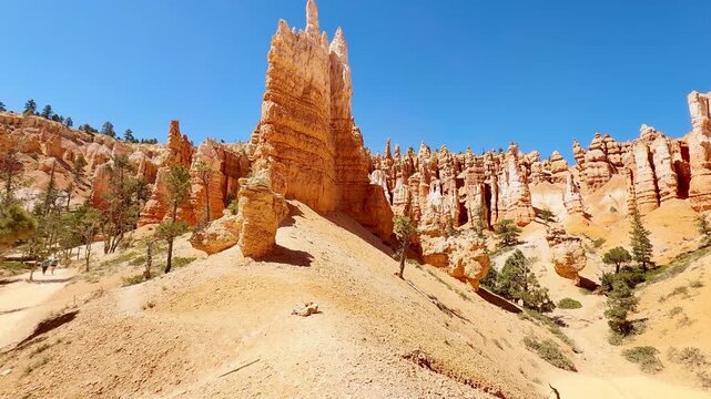 A smooth cinematic low angle shot panning across unique red rock spires resembling chess pieces or statues in Bryce Canyon, Utah. Scenic hiking trails and rare pine trees under a clear blue sky.