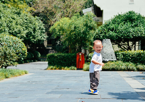 Full length shot of a cute two-year-old Chinese toddler boy running and playing outdoors at Park Hyatt Ningbo, Ningbo, Zhejiang, China