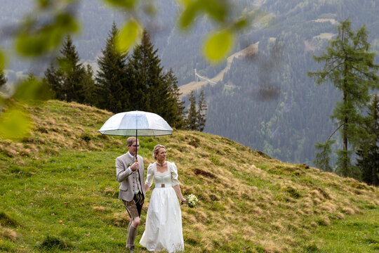 Bride and groom walking in Austrian Alps with umbrella
