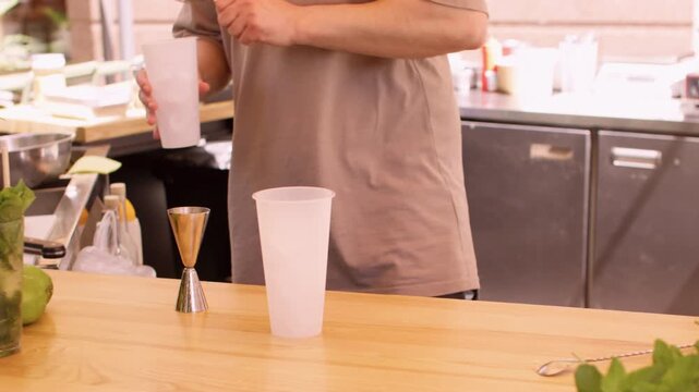 Lime beverage preparing. Tropical drink. Unrecognizable professional barman hands pouring alcohol using tool strainer for fruit fresh syrup in cafeteria.