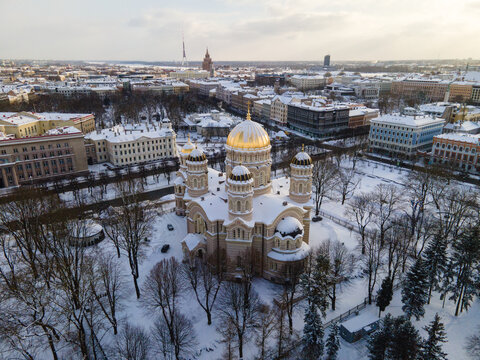 Aerial view of the Riga Nativity of Christ Orthodox Cathedral surrounded by snow-covered trees and urban architecture in Riga, Latvia.