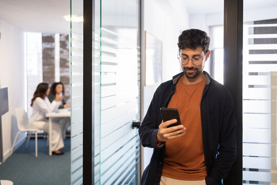Young professional using smartphone in modern office corridor