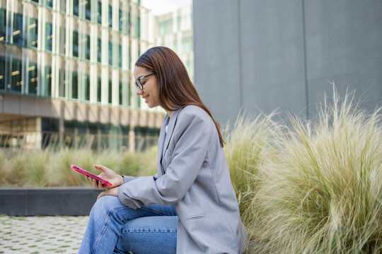Woman sitting outdoors using smartphone with building