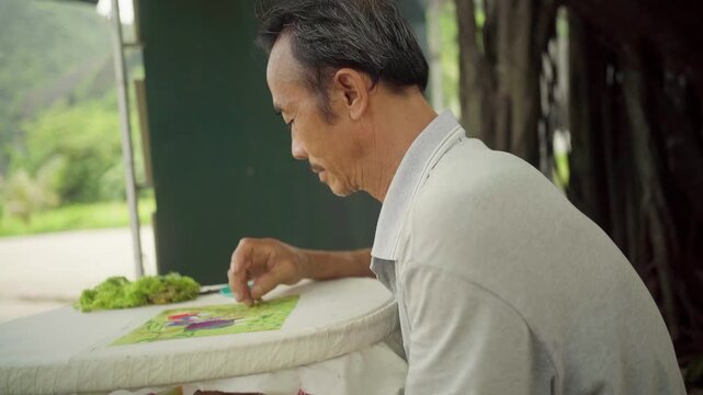Side view of an expert vietnamese tailor carefully hand stitching a colorful embroidery piece