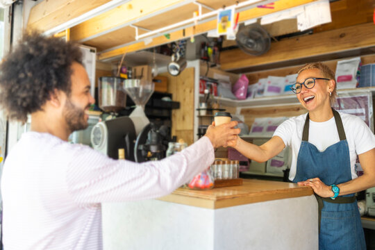 Smiling barista serving takeaway coffee at small kiosk