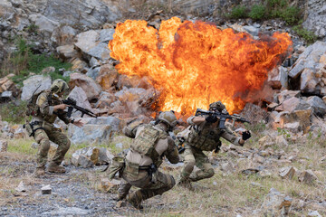 Fototapeta premium Military participate in a patrol in rocky terrain with explosion during combat scenario