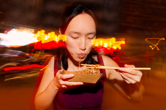 Asian woman eating street noodles at night market