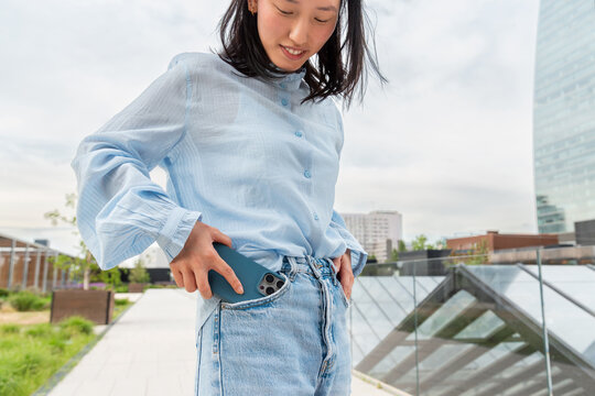Gen Z Asian woman taking smartphone from jeans pocket