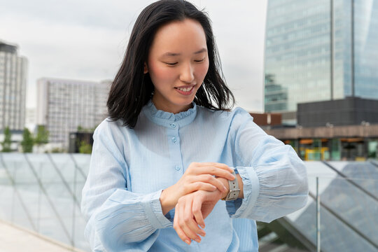 Gen Z Asian woman checking smartwatch in modern city