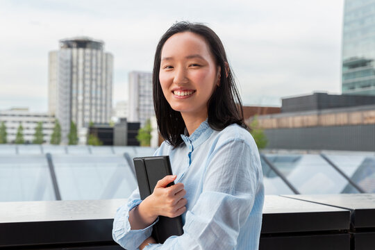 Gen Z Asian woman holding notebook on urban rooftop