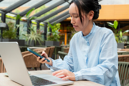 Gen Z Asian woman using smartphone and laptop at cafe