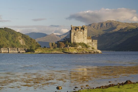 A picturesque castle on an island in the water, surrounded by mountains and a slightly cloudy sky, with dramatic mountains in the background, Eilean Donan Castle, Highlander, film set, Scotland, Great Britain