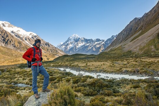 Hiker standing on a rock, Hooker Valley overlooking snow-capped Mount Cook, Hooker River, snow-capped Mount Cook National Park, Southern Alps, Canterbury, South Island, New Zealand