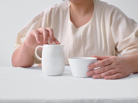 Woman holding ceramic cup and milk jug on white table
