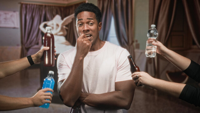 Man biting fingernail with arms crossed while multiple hands offer bottles in studio; peer pressure uncertainty.