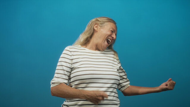 Senior woman with striped shirt, mouth open and hair whipping as she air guitars and headbanging in studio; joy.