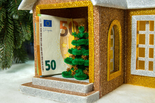 A Christmas house with a euro banknote and a Christmas tree on the porch