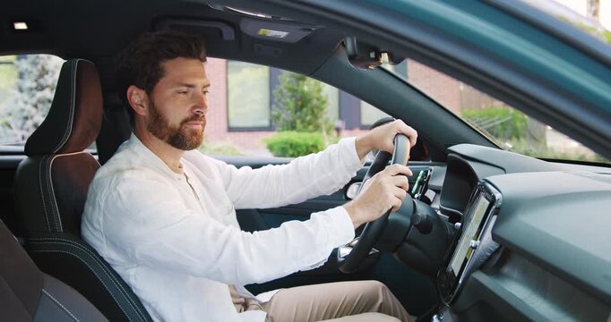 Handsome smiling man sitting inside a modern car, setting a navigation route while looking at the camera.