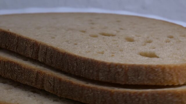 Close-up of three slices of rye bread rotating on a white plate, showcasing their soft crumb and textured crust under bright studio lighting.