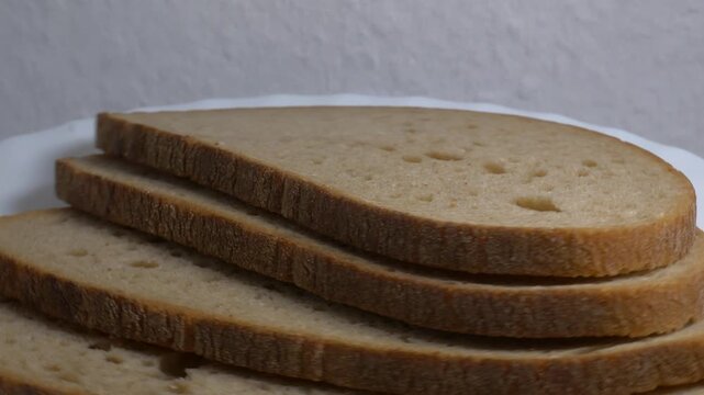 Close-up of three slices of rye bread rotating on a white plate, showcasing their soft crumb and textured crust under bright studio lighting.