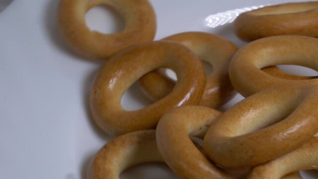 Close-up of a pile of small ring-shaped bread rolls rotating on a white plate, showcasing their smooth golden-brown crust under bright studio lighting.