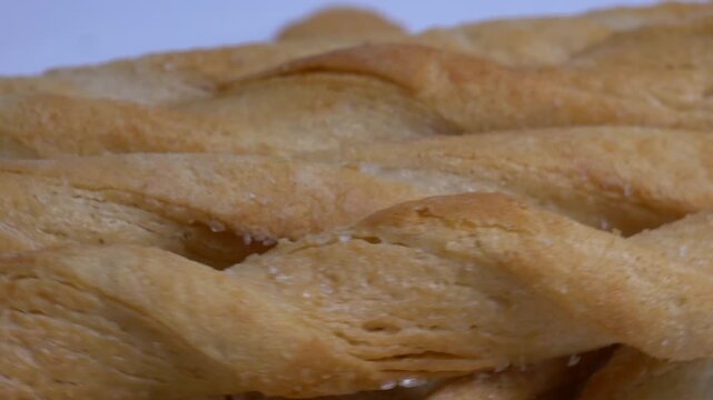 Close-up of crispy twisted puff pastry breadsticks rotating on a white plate, showcasing their golden flaky texture under bright studio lighting.