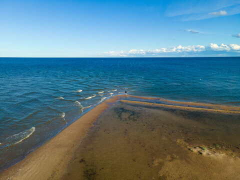 Aerial view of Cape Kolka where the Baltic Sea and the Gulf of Riga meet, featuring a sandy spit and a lone person standing at the tip in Kolka, Talsi Municipality, Latvia.