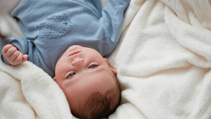 Newborn boy lying on plush white blanket on bed, knit onesie, head turned with gentle gaze and tiny fists visible in studio  innocence calm. © Krakenimages.com