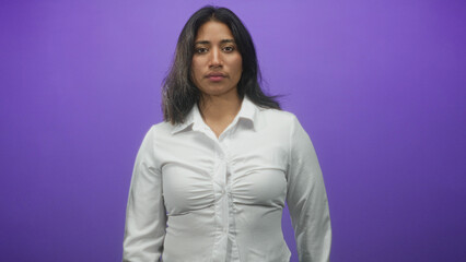 Obraz premium Woman bare face in white shirt standing facing camera in purple studio backdrop with frontal pose; calm presence.
