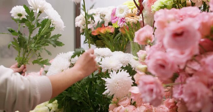 Flower composition. Seasonal floristry. Woman floral designer hands arranging eustoma chrysanthemum creating bouquet in botanical atmosphere.