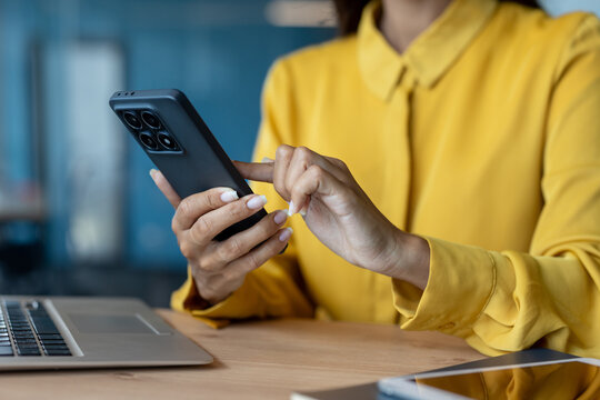 Close-up photo of female young hands in a yellow shirt wearing corsets and typing on a mobile phone