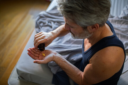 Man taking vitamin pills in bedroom at home