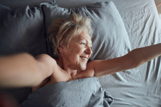 Smiling senior woman stretching in bed at home