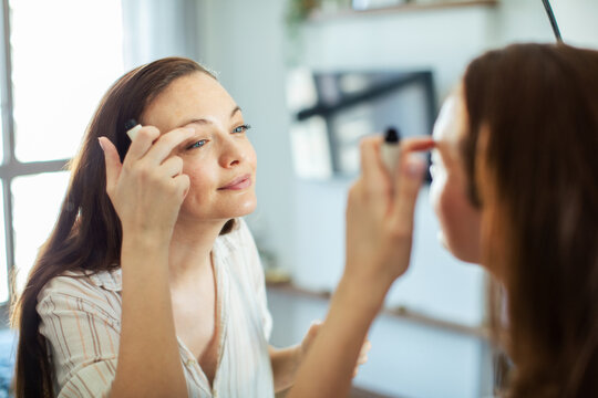 Smiling woman applying eye makeup at home mirror