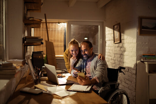 Smiling couple managing finances in home office at night, man in wheelchair