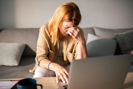 Stressed woman with headache working on laptop at home