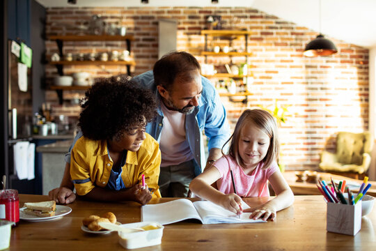 Father helping children with homework in a home kitchen