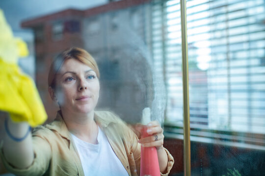 Woman cleaning window with spray and cloth at home