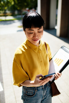 Businesswoman checking smartphone outdoors with reports